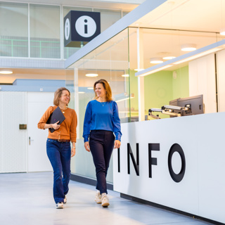 Foto van twee collega's van Dudok Wonen die langs de infobalie in de Melkfabriek lopen