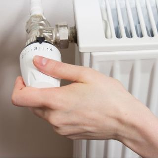 Close-up van een hand die aan de draaiknop van een verwarming draait. De foto wordt gebruikt als sfeerfoto bij een artikel over energie besparen.